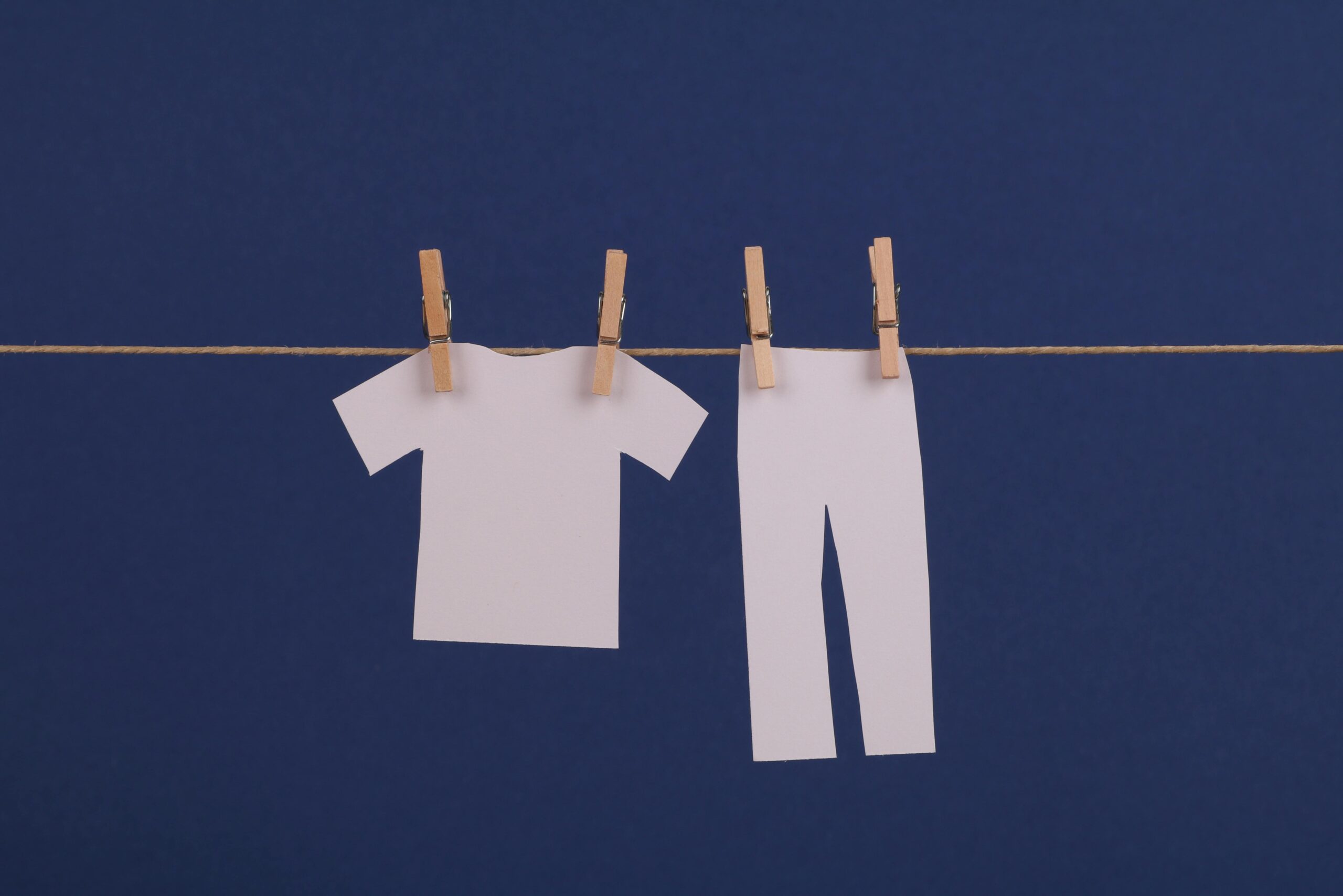 Minimalist design of cut out paper clothes hanging on a string against a blue background.